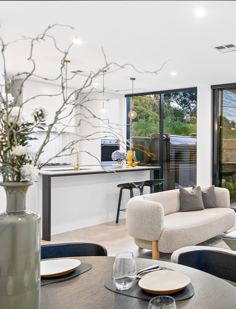 Open plan living and kitchen with soft white colour scheme with vase in the foreground