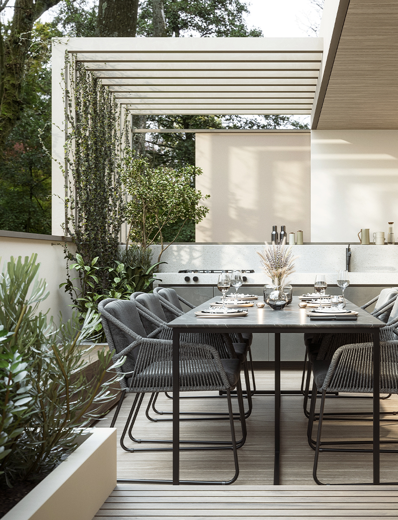 Modern home terrace. Luxury outdoor table with chairs and built in barbeque with dappled light from surrounding trees.