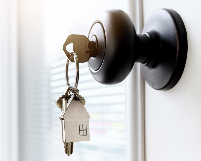 Close up shot of black rounded door handle with key inserted - from the key set there is a metal house decorative keyring hanging down.