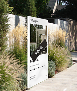 Real estate sign board with sold sticker on pathway with native grasses